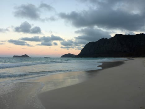 The tranquil beauty of Waimanalo Beach unfolds as the sun gracefully dips below the horizon. Cobalt blue waters gently kiss the sandy shore, while the silhouettes of palm trees stand tall against the colorful sky. A moment of serenity captured in the heart of Hawaii.