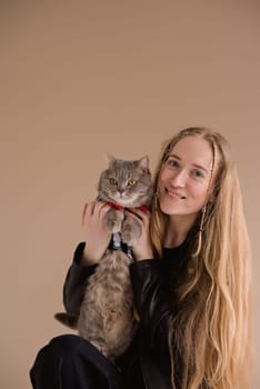 A woman natural blonde smiling in a black clothes stand, sitting on photo studio. girl with pet scottish straight cat. long hair