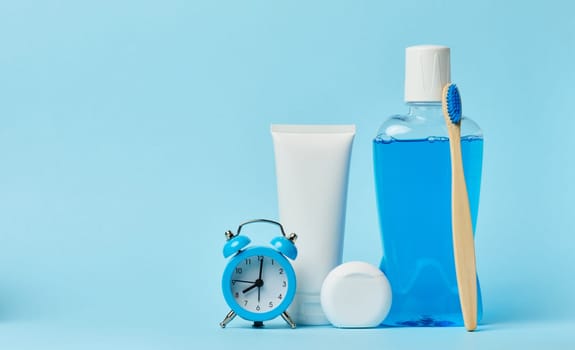 Mouthwash and toothpaste tube, alarm clock on blue background, oral hygiene