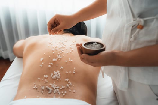 Blissful man customer having exfoliation treatment in luxury spa salon with warmth candle light ambient. Salt scrub beauty treatment in health spa body scrub. Quiescent