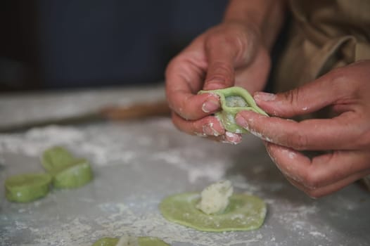 Close-up hands of a woman in the rural kitchen, sculpts dumplings from dough with mashed potatoes filling. Cooking delicious homemade vegetarian dumplings, Ukrainian varenyky or Italian ravioli