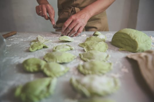 Close-up housewife preparing dumplings varenyky ravioli, standing at marble table in the rustic kitchen of a rural house. People. Culinary. Traditional Italian or Ukrainian cuisine. Domestic lifestyle