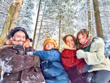 Joyful family ethnic dress with shawls and earflap hats in winter forest in carnival Maslenitsa in Russia. Tourists in Shrovetide in spring. Mother, father, son, daughter having fun in the snow