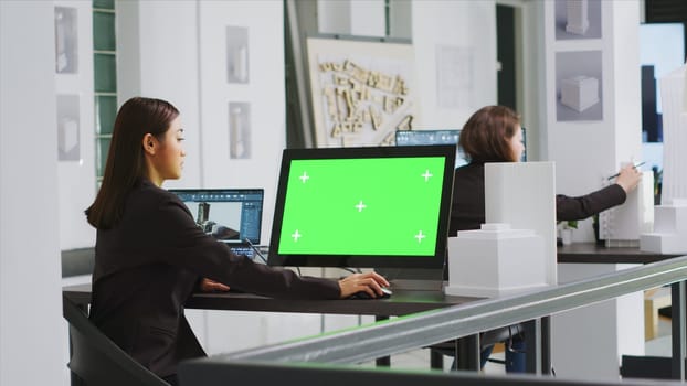 Architect using computer with greenscreen at workstation in agency office, looking at blank mockup template on monitor. Engineer employed at a real estate small business. Tripod shot.