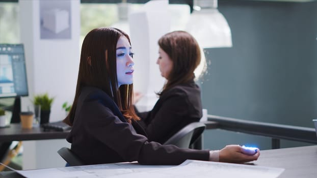 Developer talking to consultant on holographic projection in coworking space, using hologram showing engineer to discuss project blueprints. Employees review architectural process. Tripod shot.