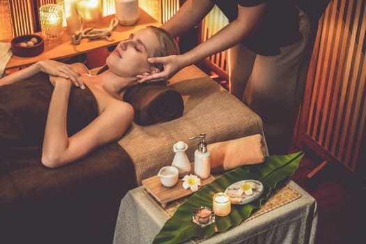 Caucasian woman enjoying relaxing anti-stress head massage and pampering facial beauty skin recreation leisure in warm candle lighting ambient salon spa in luxury resort or hotel. Quiescent