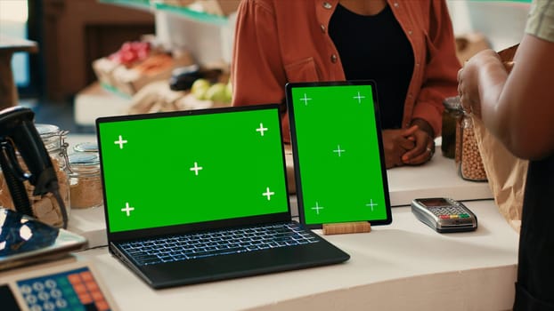 Laptop and tablet running greenscreen layout in local store, promoting sustainable lifestyle and zero waste farming. Vendor at checkout uses devices with chromakey display isolated mockup.