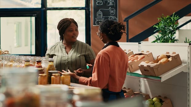 Local storekeeper recommends grains and homemade sauces to loyal customer, ensuring organic source of proteins for goods in jars. Merchant presenting new ecological nonpolluting merchandise.