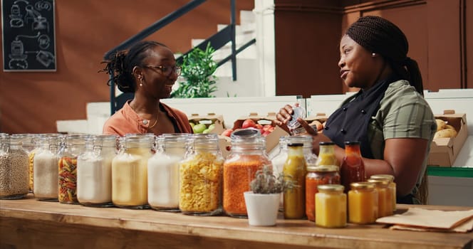 African american seller giving food sample to customer, presenting new homemade snacks with natural ingredients. Vegan woman trying out market products before buying. Handheld shot.