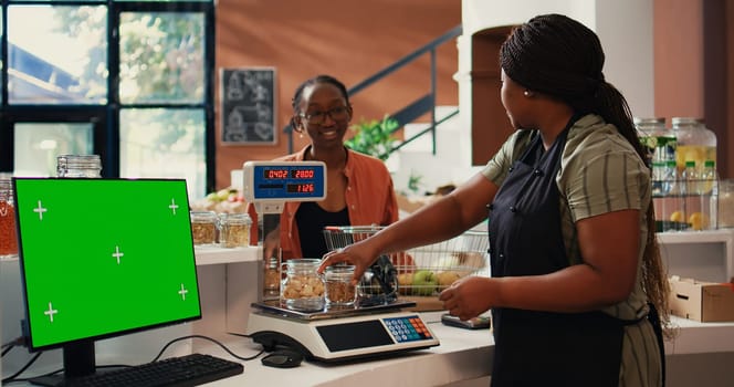 Shopper purchasing goods next to greenscreen on monitor, isolated mockup template on pc at cash register in supermarket. Vendor working with display running copyspace layout. Tripod shot.