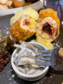 Chicken cordon bleu dish, crispy fried rolled chicken breast stuffed with cheese and ham melted in cream along with salad and mash potatoes served in brown plate