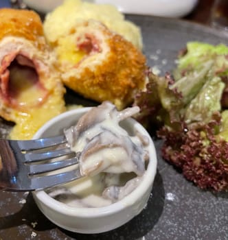 Chicken cordon bleu dish, crispy fried rolled chicken breast stuffed with cheese and ham melted in cream along with salad and mash potatoes served in brown plate
