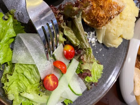 Chicken cordon bleu dish, crispy fried rolled chicken breast stuffed with cheese and ham melted in cream along with salad and mash potatoes served in brown plate