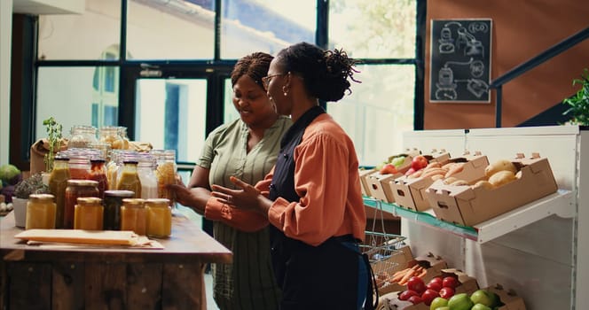 Merchant presenting homemade sauces and spices to client, promoting local farming and healthy eating. Storekeeper recommending bio organic bulk products at supermarket. Handheld shot.