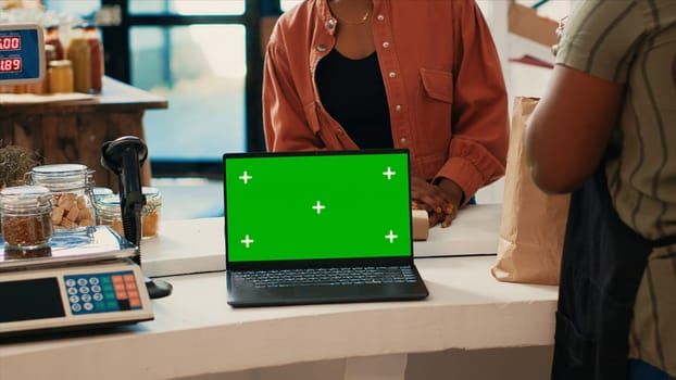 Shopper buying organic goods next to greenscreen on pc, waiting for bag with ripe freshly harvested products at zero waste store checkout. Laptop running isolated mockup copyspace layout.