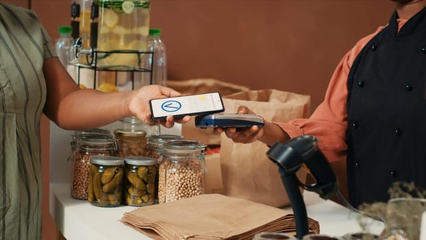 African american woman buying fresh bio produce with nfc mobile payment at pos, supporting sustainable lifestyle and healthy eating. Shopper looking for organic homegrown fruits and vegetables.