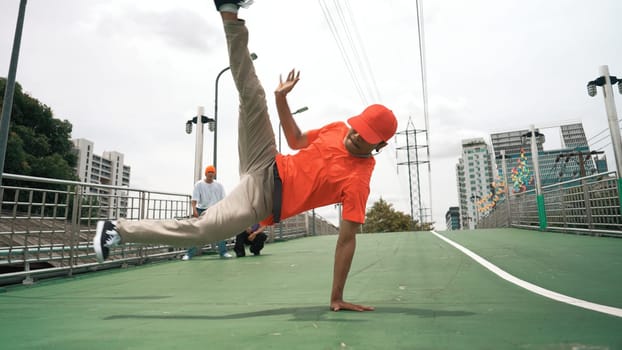 Young happy hipster perform break dancing or foot step with friend moving to hiphop music together. Skilled dancer doing freeze pose and waving hand. Modern lifestyle. Outdoor music 2024. Sprightly.