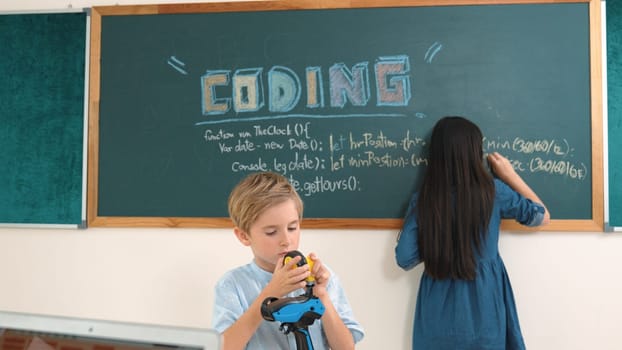 Caucasian elementary student fixing machine model at STEM class. Attractive cute student standing blackboard while writing coding engineering prompt and programing AI software at STEM class. Pedagogy.