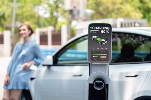 Electric vehicle recharging battery from home EV charging station using alternative energy with net zero emission on blurred background of young girl charging her car before vacation travel. Perpetual