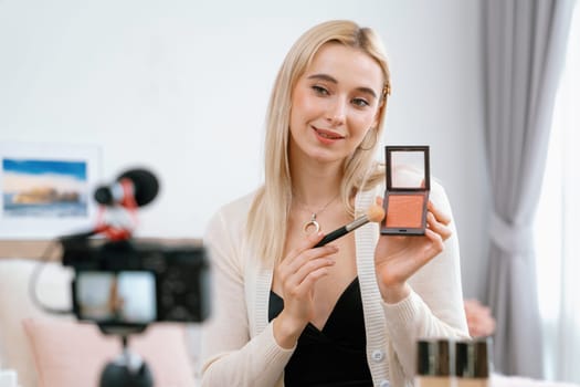 Young woman making beauty and cosmetic tutorial video content for social media. Beauty blogger smiles to camera while showing how to beauty care to audience or followers. Blithe