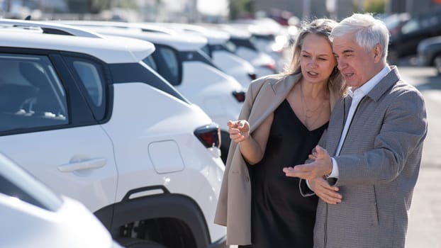 Mature Caucasian couple walks past cars outdoors, choosing a new one