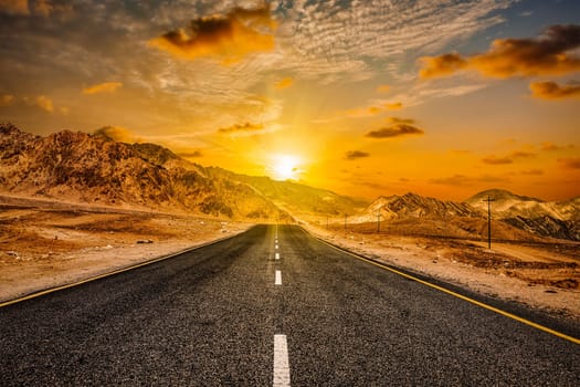 Travel forward concept background - road in Himalayas with mountains and dramatic clouds on sunset. Ladakh, Jammu and Kashmir, India