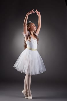 Graceful little ballerina posing on gray backdrop