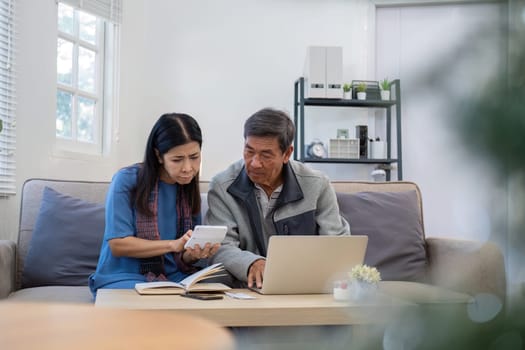 Retired Asian couple in their 60s Feeling stressed while calculating monthly expenses on the living room sofa..