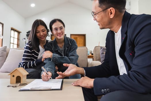 Asian couple looking at house plans and talking with a real estate agent about signing documents for purchase of a new home..