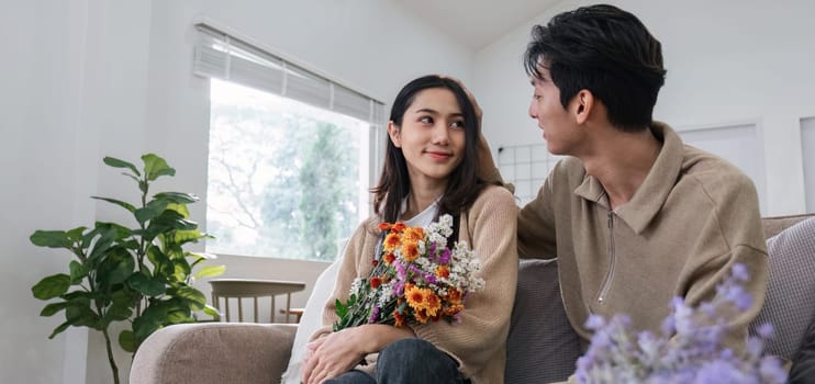 Young couple hugging and showing their love to each other. And give bouquets of flowers to each other on special days or Valentine's Day. On the sofa in the living room.