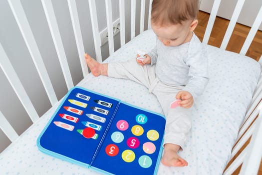 A happy baby is sitting in a crib playing with a felt board. Its a joyful leisure event