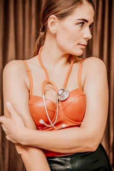 Young woman in red corset and black leather pants with a phonendoscope. Sexy brunette nurse in red and black costume with a stethoscope in her hands. Role doctor play. Entertainment