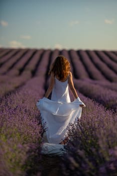 Back view woman lavender sunset. Happy woman in white dress holds lavender bouquet. Aromatherapy concept, lavender oil, photo session in lavender.