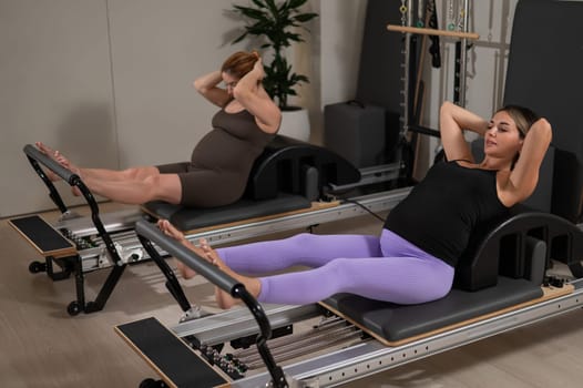 Two pregnant women do Pilates exercises on a reformer. Yoga class for pregnant women