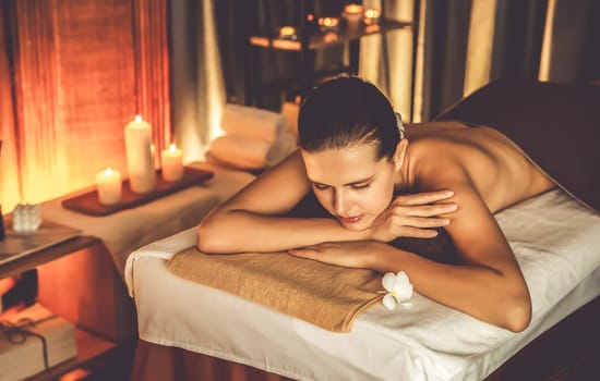 Caucasian woman customer enjoying relaxing anti-stress spa massage and pampering with beauty skin recreation leisure in warm candle lighting ambient salon spa at luxury resort or hotel. Quiescent