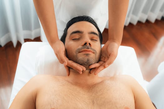 Caucasian man enjoying relaxing anti-stress head massage and pampering facial beauty skin recreation leisure in dayspa modern light ambient at luxury resort or hotel spa salon. Quiescent