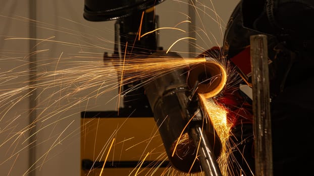 A welder wearing a protective mask cuts a metal pipe