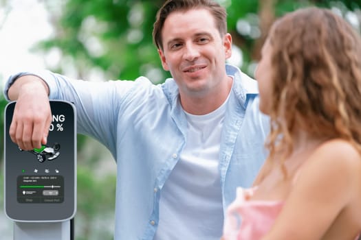 Happy and lovely couple with eco-friendly conscious recharging electric vehicle from EV charging station. EV car technology utilized as alternative transportation for future sustainability. Synchronos