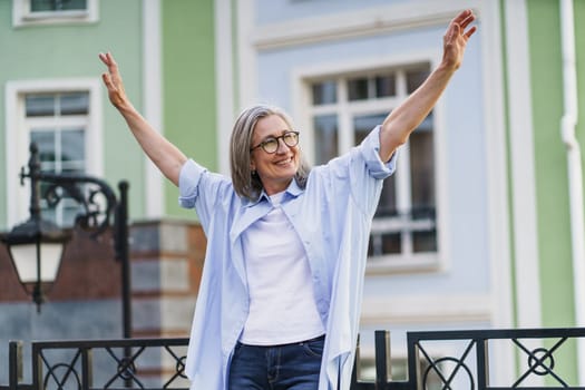 A woman standing in front of a building, arms outstretched.