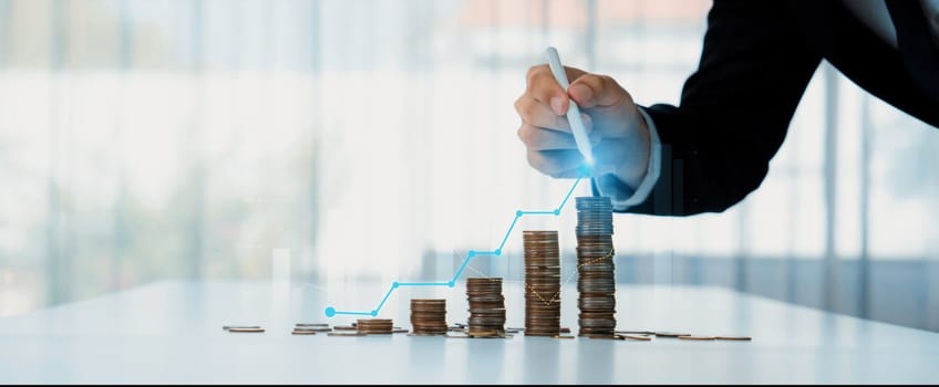 Coin stack with digital graphic indicator symbolizing business investment and economic growth. Businessman doing financial planning to achieve financial goal and contribute to profit. Shrewd