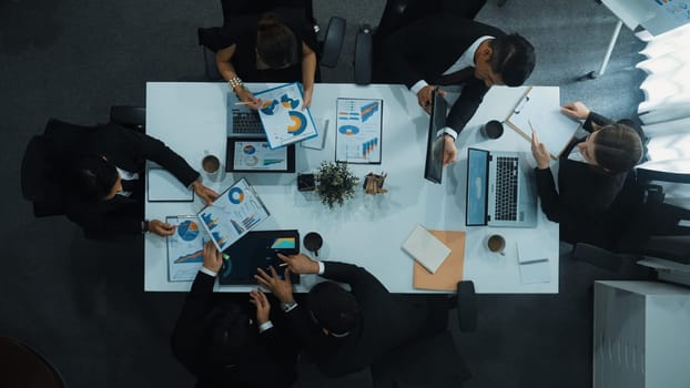 Top down aerial view of business people discussing about financial strategy on table with document and tablet display investment statistic at meeting. Diverse team brainstorm about plan. Directorate.