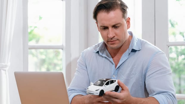 Car design engineer analyze car model prototype for automotive business company at home office. Vehicle designer holding scale car, carefully analyzing looking for any flaw or improvement. Synchronos