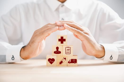 Wooden cube block displaying healthcare icons, topped by a doctor hand indicating protection, exemplifying healthcare and insurance concept. Building a secure medical future. Health care concept