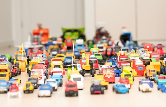 Toy cars, motorcycles, tractors, buses, pickups, many colorful small and large cars are arranged for play on the floor in the children's room. Childhood concept. soft focus.