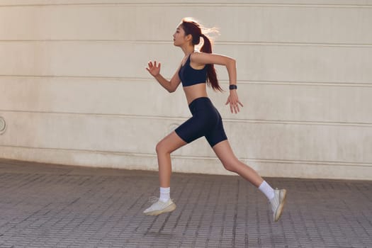 Young woman in sportswear is running on modern buildings background. Active lifestyle concept