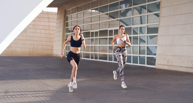 Active women athlete running on sunny morning side by side on modern building background
