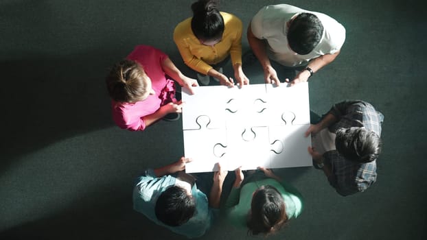 Top down view of business people gathering jigsaw together at meeting. Aerial view of diverse team collect or put piece of jigsaw puzzle together and standing while wearing casual cloth. Symposium.