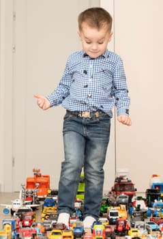 Children. Toy cars. A small cheerful and handsome boy, 4 years old, wearing a checkered shirt, plays with many colorful cars in a home interior. The toys are placed evenly on the floor.