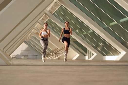 Two athletic women in sportswear is jogging around the city in early morning. Reaching the goal