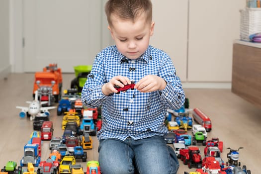 Concept of children's toys. A little boy, 4 years old, enthusiastically plays, sitting on the floor, with multi-colored small and large cars in the children's room. Soft focus